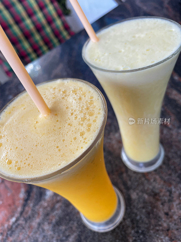 Close-up image of glasses of alcoholic ‘Piña colada’ cocktail and Orange Juice non-alcoholic drink with drinking straws on kitchen counter, elevated view,  focus on foreground